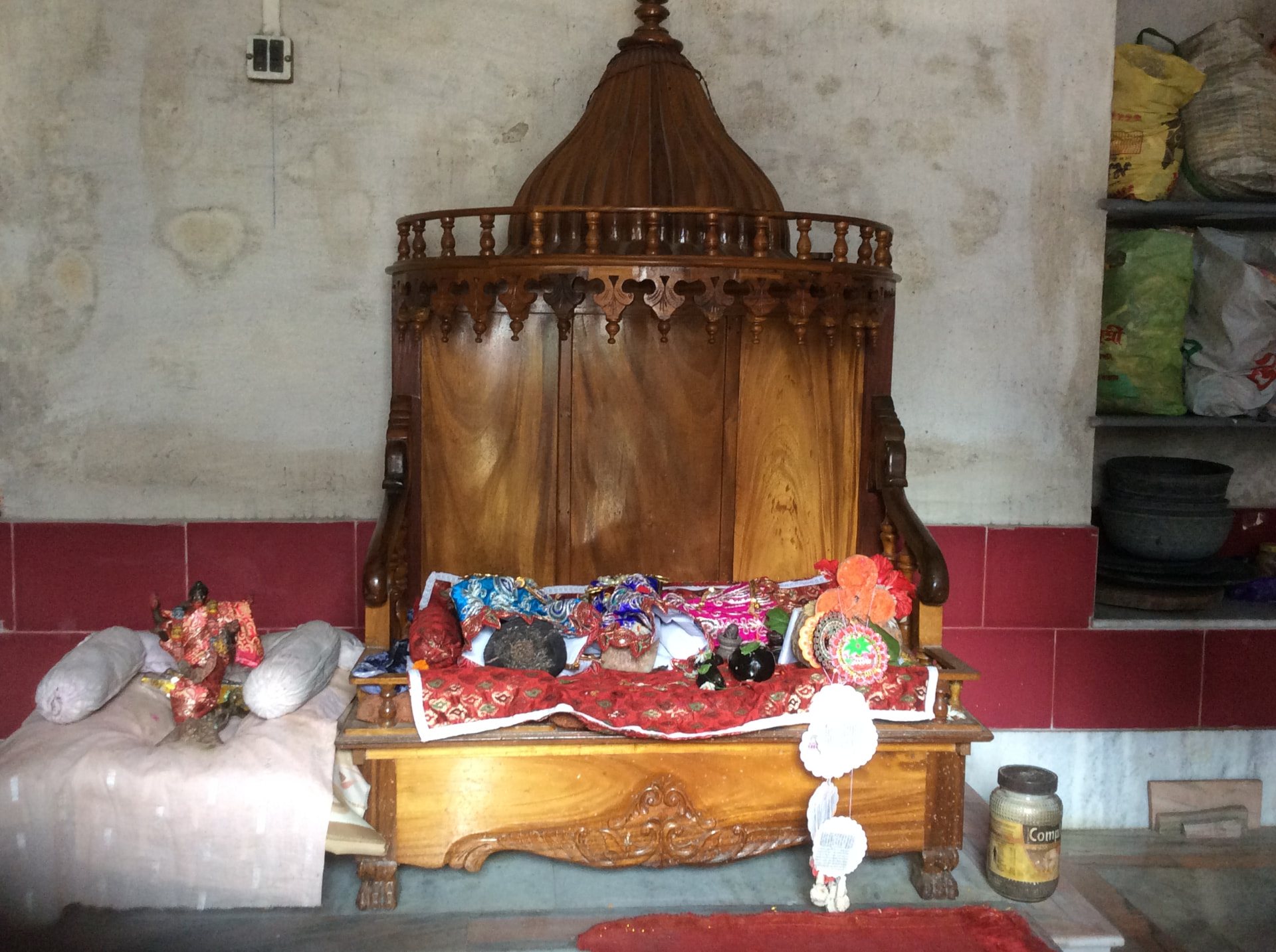 A carved wooden throne with a domed canopy, the deities resting on it under red and gold cloths with flowers