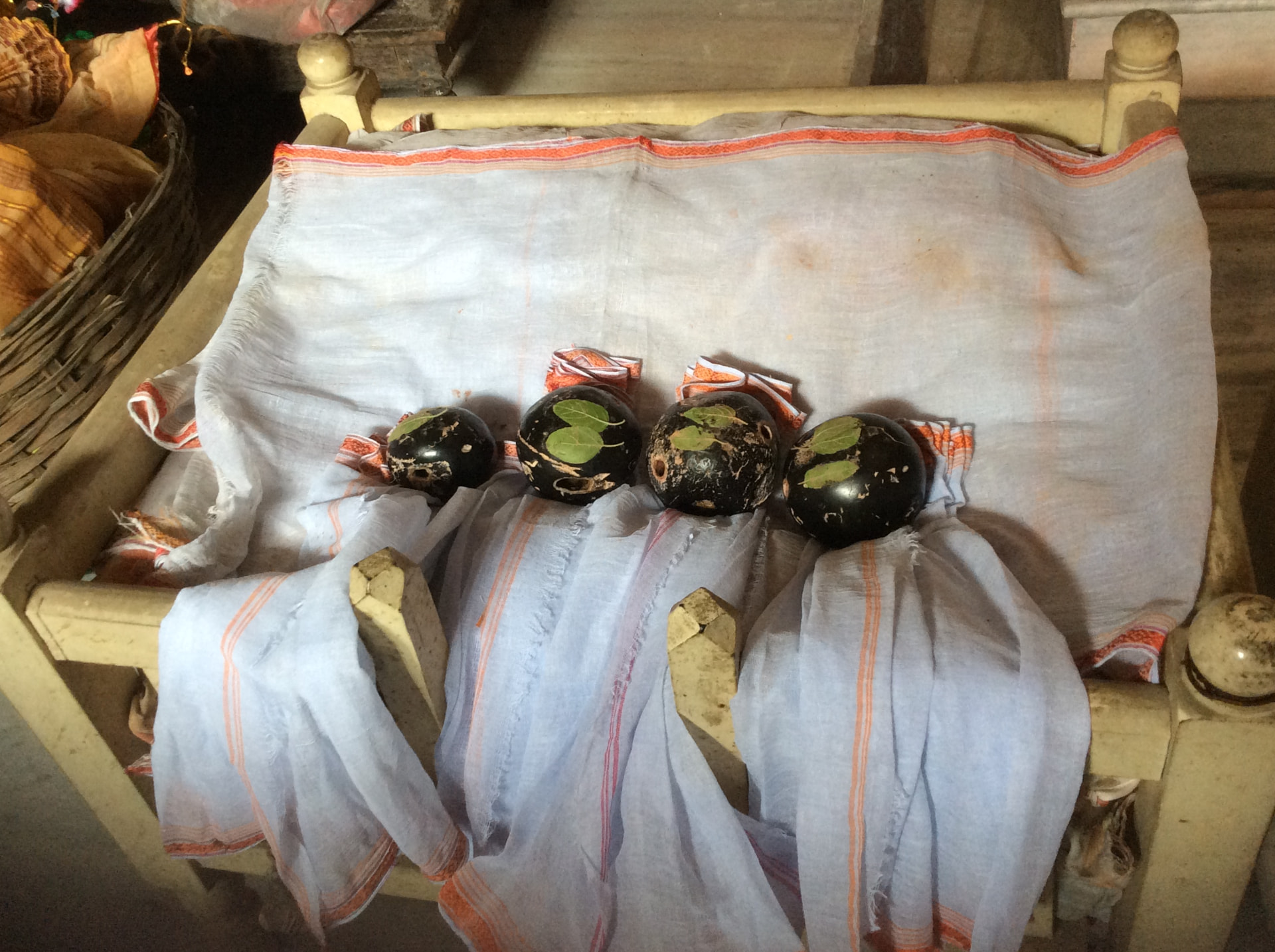 Four round black sacred stones in a row on a small wooden bed, each with tulsi leaves on top and wrapped in white cloth